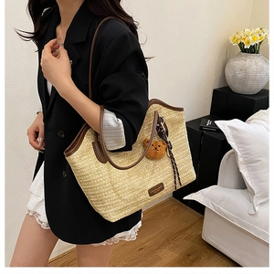 Detail of woven straw tote bag with brown leather trim and cute teddy bear pendant
