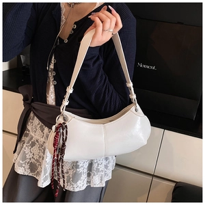 Close-up of a white crescent shoulder bag with a decorative brown braided charm