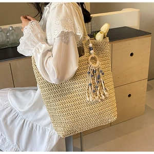 Detail of woven straw tote bag featuring bohemian tassel charm and evil eye beads