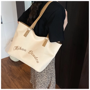 Dettaglio borsa tote in tela beige con manici in pelle marrone e scritta artistica