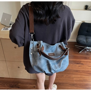 Dettaglio della borsa tote in denim blu con manici marroni e tracolla regolabile