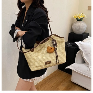 Detail of woven straw tote bag with brown leather handles and a plush bear charm