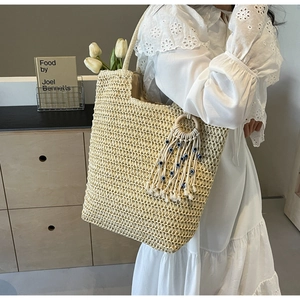 Close-up of beige woven tote bag with blue evil eye tassel charm and fringe detail