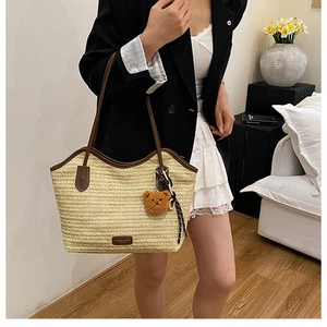 Detail of woven straw tote bag featuring brown leather trim and a cute plush bear charm