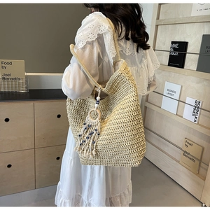 Close-up of beige woven tote bag with a blue beaded tassel charm and fringe detail