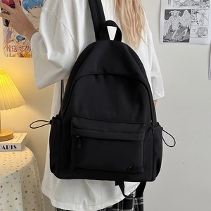 Dettaglio dello zaino in nylon nero che mostra il logo ricamato e la tasca con zip
