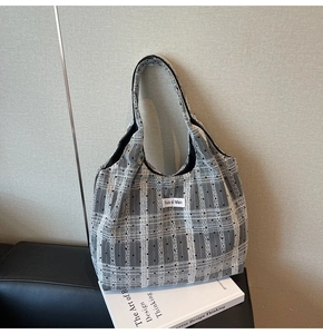Détail du sac cabas en toile à carreaux gris sur un canapé en cuir avec livre