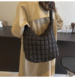 Close-up of a black quilted tote bag with a pleated design worn on a model's shoulder