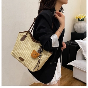 Detail of beige straw tote bag featuring brown leather straps and a cute teddy bear charm