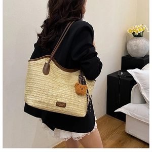 Detail of beige straw tote bag with brown leather handles and cute plush bear charm