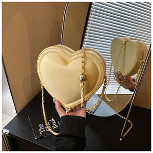 Dettaglio della borsa a tracolla color crema a forma di cuore con catena dorata e zip