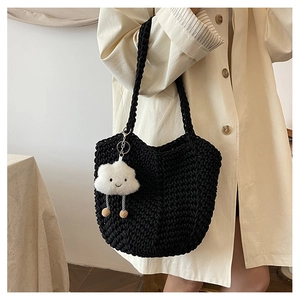 Detail of black woven tote bag with a white cloud plush charm in a lifestyle setting