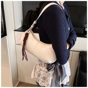 Detail of a creamy white half-moon hobo bag with a red and black woven tassel charm