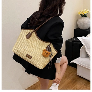 Detail of beige woven straw tote with brown leather handles and a plush bear pendant