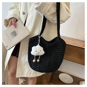 Detail of hand-woven black tote bag with white cloud plush charm held by a model