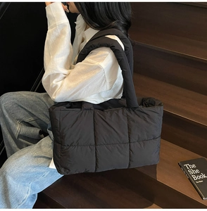 Detailed view of black quilted down tote bag worn on shoulder by model on stairs