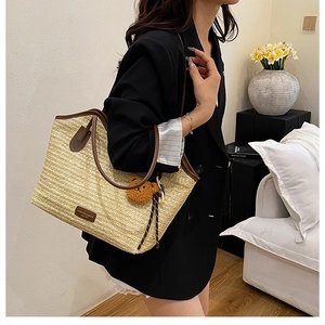 Detail of woven straw tote bag featuring brown leather trim and cute bear charm accessory
