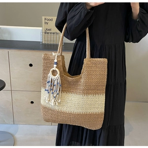 Detail of hand-woven straw tote bag with evil eye tassel charm and striped texture