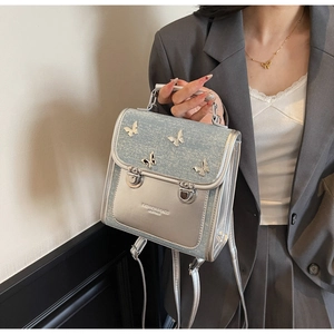 Detail of silver metallic leather and denim backpack with 3D metal butterfly ornaments