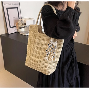 Detail of woven beige tote bag featuring cotton tassels and evil eye charm on shoulder strap