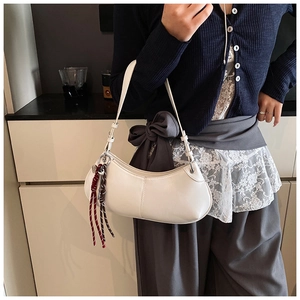 Detailed close-up of a white minimalist crescent bag with woven fringe charm on a model