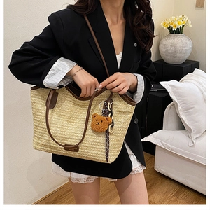 Detail of beige straw tote bag with brown leather trim and cute teddy bear charm