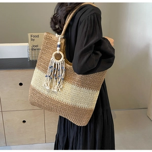 Close-up of woven straw tote bag featuring blue evil eye tassel charm and boho fringe details