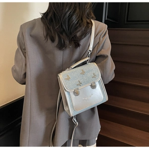 Detail of silver square crossbody bag with metal butterfly charms on a grey blazer