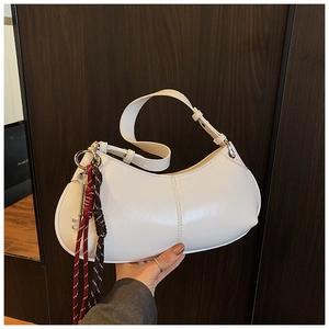 Detailed close-up of a white crescent shoulder bag with braided rope charm and stitch detail