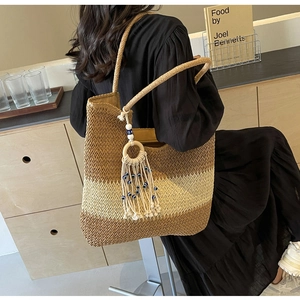 Detail of a large woven straw tote bag with three-tone color blocks and evil eye tassels