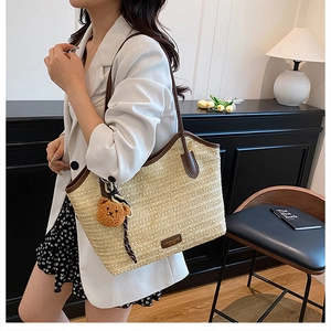 Detail of beige straw tote bag with brown leather handles and cute bear charm pendant