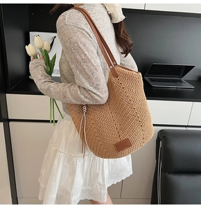 Detail of woven straw tote bag with brown leather handles and brand patch on front