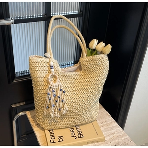Detail of woven straw tote bag with beaded tassel charm and blue eye accent