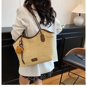 Detail view of woven straw tote bag with brown leather handles and plush bear charm