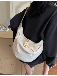Large beige nylon crescent bag with floral embroidered strap shown on a model