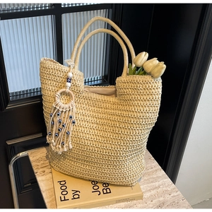 Close-up of beige woven tote bag with blue evil eye tassel and fresh white tulips