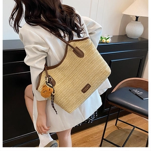 Close-up of large straw tote bag featuring brown leather trim and a cute teddy bear charm