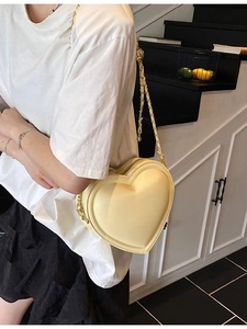 Borsa a tracolla alla moda a forma di cuore in pelle crema con catena dorata indossata dal modello