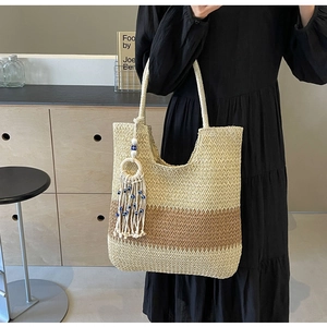 Close-up of woven straw tote bag featuring contrast stripes and evil eye tassel detail