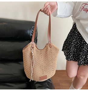 Detail of beige woven tote bag with V-shaped texture, brown faux leather handles and tassel
