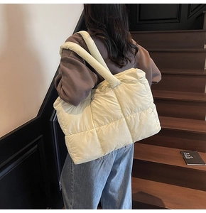 Detailed side view of large beige quilted down tote bag worn on shoulder for commute