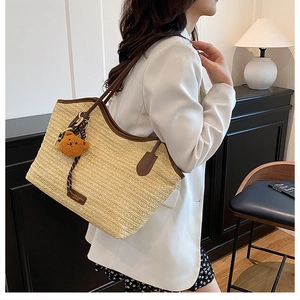 Detail of beige woven tote bag featuring brown leather trim and cute plush bear charm