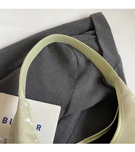 Detail view of the wide smooth shoulder strap on a light green glossy tote bag