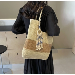 Detail of woven tote bag with bohemian tassel and blue eye charm on female model