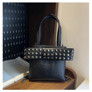 Détail de sac seau noir en cuir grainé avec un nœud à rivets et bandoulière chaîne
