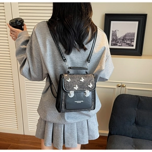 Detail of black tweed backpack with 3D white butterflies and silver hardware