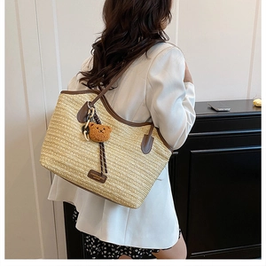 Detail of straw woven tote with brown leather handles and a plush bear charm accessory