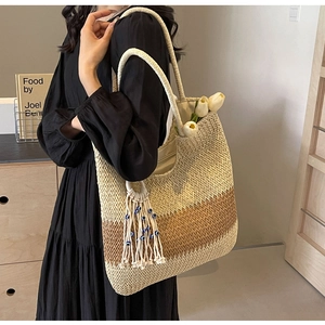 Detail of woven straw tote bag featuring gradient stripes and handmade evil eye fringe charm