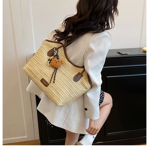 Detail of woven straw tote bag with brown leather handles and a plush bear pendant