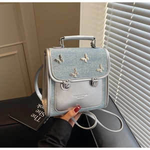 Detail of silver butterfly ornaments and buckle closure on a chic denim拼接 backpack